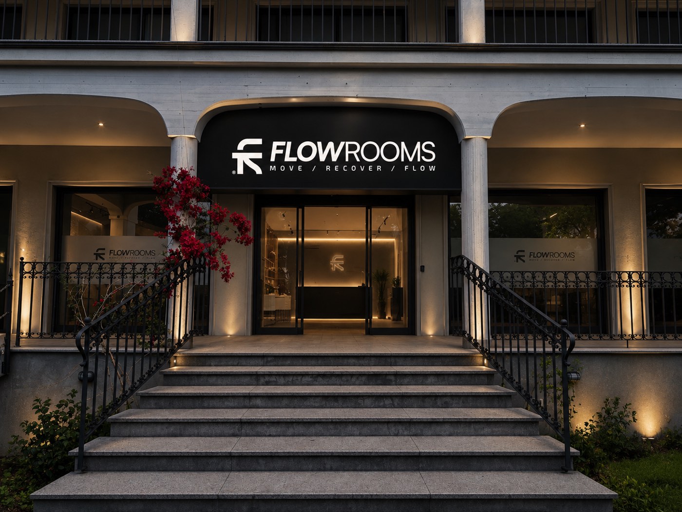 L’ingresso illuminato di FlowRooms di sera, con l’insegna sopra la scala